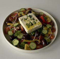 a white bowl filled with lots of different types of vegetables and cheese on top of it