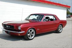 an old red mustang parked in front of a building