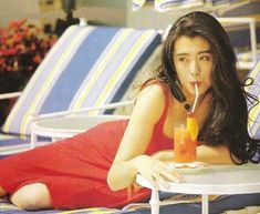 a woman in a red dress is sitting on a beach chair with a glass of orange juice