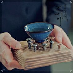 a person holding a small blue bowl on top of a wooden stand with metal knobs