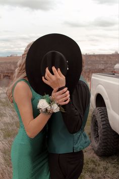 a man in a black hat hugging a woman wearing a green dress and holding a flower