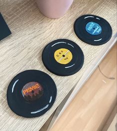 three black records sitting on top of a wooden table next to a pink cup and laptop