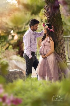 a pregnant woman standing next to a man near a tree