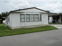 a small white house sitting on the side of a road next to a grass covered field