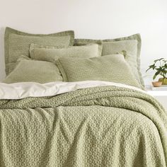 a bed with green bedspread and pillows on top of it next to a potted plant