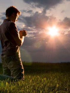 a man standing on top of a lush green field under a cloudy sky with the sun behind him