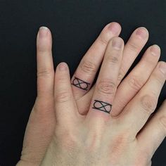 two hands with tattoos on their fingers holding each other's fingers and one has the letter