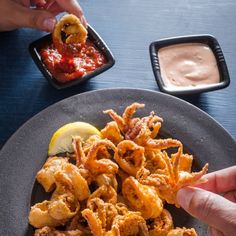 a plate full of fried food with dipping sauce on the side and two hands reaching for it