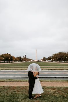 a bride and groom standing under an umbrella in front of the washington monument