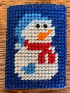 a blue and white needled coaster with a snowman design on it, sitting on a wooden surface