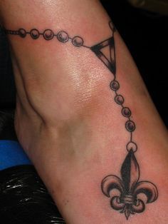 a woman's foot with a black and white tattoo design on it, featuring a fleur de lis