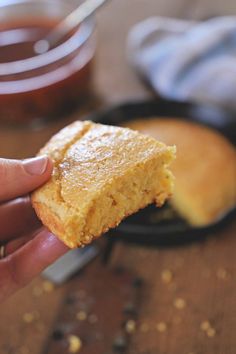 a hand holding a piece of cake in front of a skillet with peanut butter on it