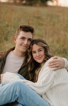 a young man and woman are sitting on the ground in front of some tall grass