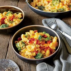 two bowls filled with macaroni and broccoli on top of a wooden table