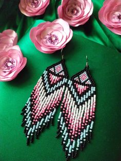 pink and blue beaded owl earrings on green fabric with flowers in the background,