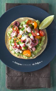 a taco on a blue plate with a lime wedge next to it and a napkin