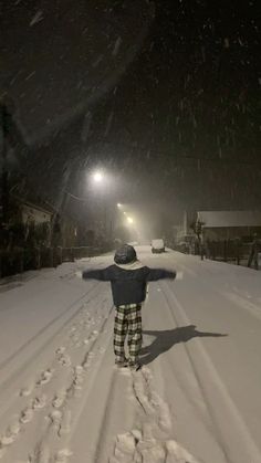 a person standing in the middle of a snow covered road at night with their arms outstretched