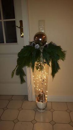 a vase filled with greenery and lights on top of a tiled floor next to a door