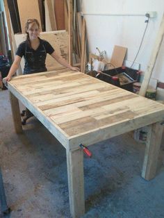 a woman standing next to a table made out of wooden planks in a workshop