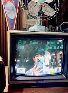 an old television sitting on top of a wooden table next to a fan and remote control