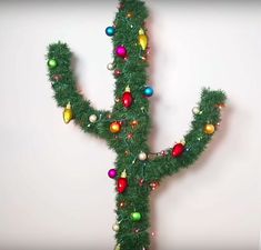 a cactus made out of christmas ornaments on a white wall with the letter y spelled out