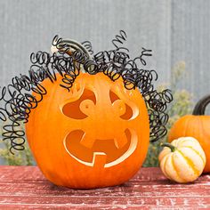 a carved pumpkin sitting on top of a table next to two small pumpkins with hair in the shape of a face