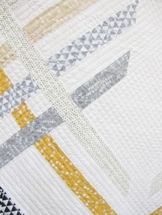 a close up view of a quilt on a table top with yellow, grey and white designs