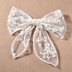 a white lace bow with snowflakes on the front and bottom, sitting on a beige background