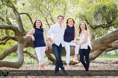 three women and one man are posing for a photo in front of a large tree