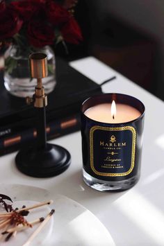 a lit candle sitting on top of a table next to a plate and vase with flowers