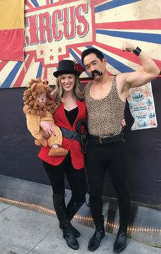 a man and woman dressed in costumes posing for a photo with a circus sign behind them