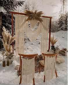 two wooden chairs sitting in the snow next to a white wall hanging from it's side