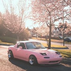 a pink sports car parked on the side of the road in front of some trees