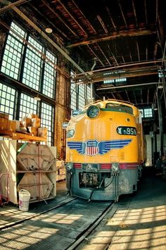 a yellow train is parked in an old warehouse with lots of windows on the ceiling