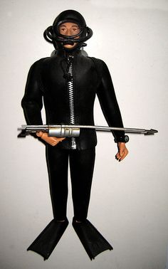 a man in a scuba suit holding a metal spear and wearing a diving helmet with his hands on the hips