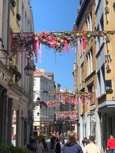 people are walking down the street in front of buildings with pink flowers hanging from them