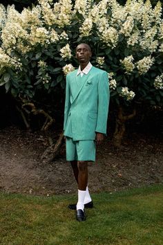 a man in a green suit and white socks standing next to a bush with white flowers