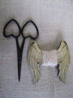 a pair of scissors sitting next to an angel wing on top of a piece of fabric