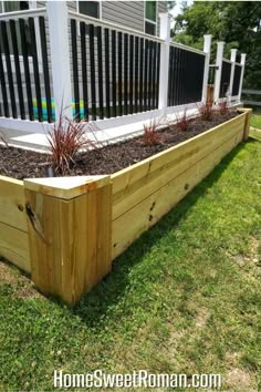 a wooden planter with plants growing in it on the grass next to a fence