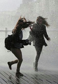 two people running in the rain, one with her back to the camera and the other holding an umbrella