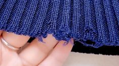 a woman's hand holding onto the edge of a blue knitted piece of cloth