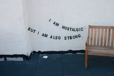 a wooden bench sitting in front of a white wall with writing on it and a brown chair next to it