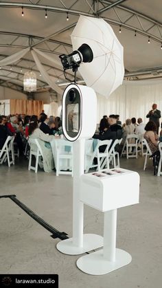 a camera set up in front of a white chair with an umbrella on it's stand