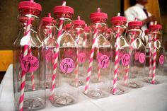 pink and white striped straws in glass bottles on a table with people standing behind them