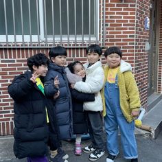 four children standing in front of a brick building with their arms around each other's shoulders