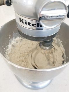 a metal bowl filled with batter on top of a white counter next to a mixer