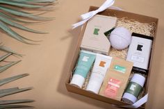 an open box containing various skin care products on a table next to palm leaves and a white ball