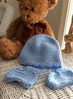 a brown teddy bear sitting on top of a bed next to a blue knitted hat