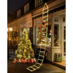 a lighted christmas tree in front of a store with a ladder lit up to look like it's going down the street