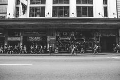 black and white photograph of people crossing the street in front of a building